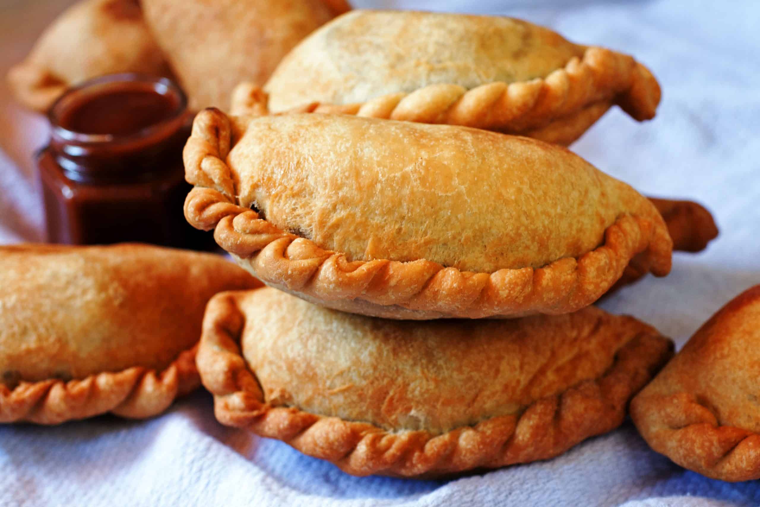 Empanada de pollo boliviana con masa dorada, partida muestra pollo con cebolla, huevo y ají amarillo.